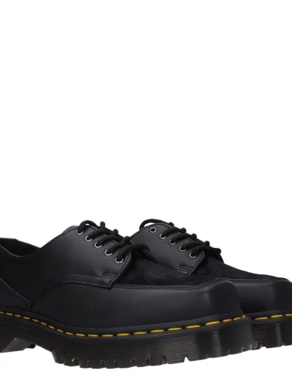 Black leather and suede chunky-soled dress shoes with yellow stitching, lace-up closure, and rugged outsole for a bold, fashionable statement.
