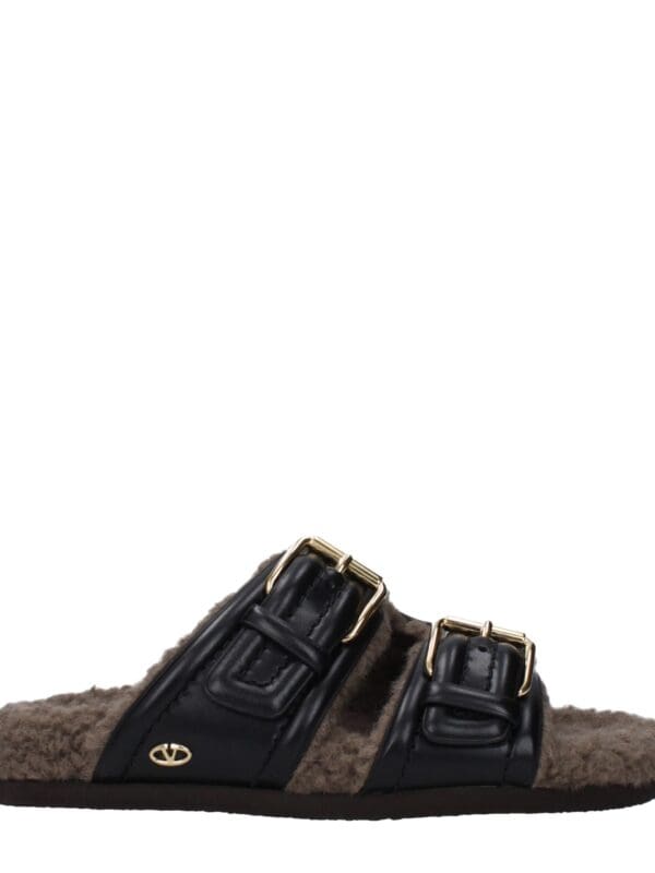 Soft plush slide slippers with black leather straps, gold buckle details, and a cozy beige lining, combining luxury style and comfort for indoor or casual wear.