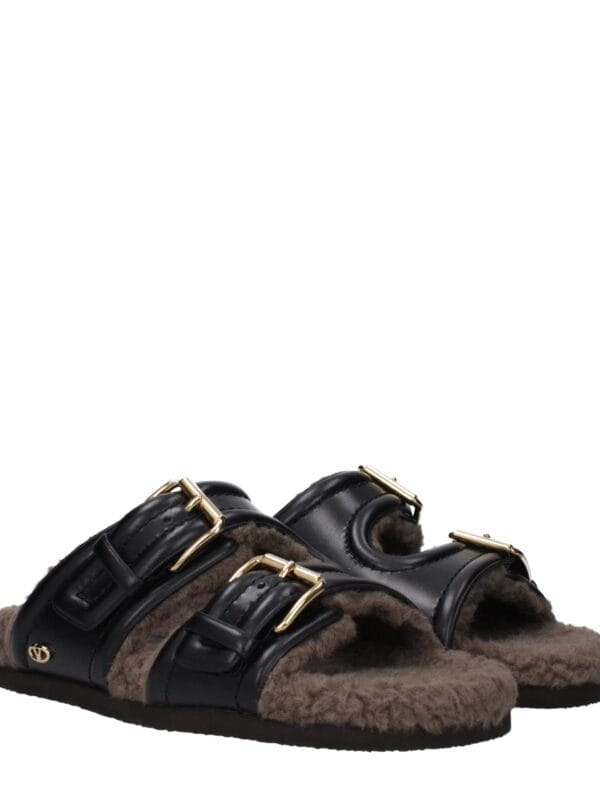 Luxurious black leather slide sandals with gold buckles and plush shearling lining, perfect for stylish comfort and cold-weather fashion.