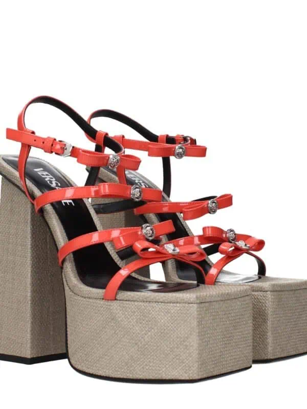 Red high-heeled platform sandals with glossy straps adorned with rhinestones and bow details, featuring beige textured block heels for a bold, stylish look.