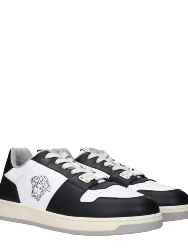 Black and white designer sneakers with a lion face logo on the side, featuring perforated toe caps, lace-up closure, and a sleek low-top style. Perfect for stylish casual wear.