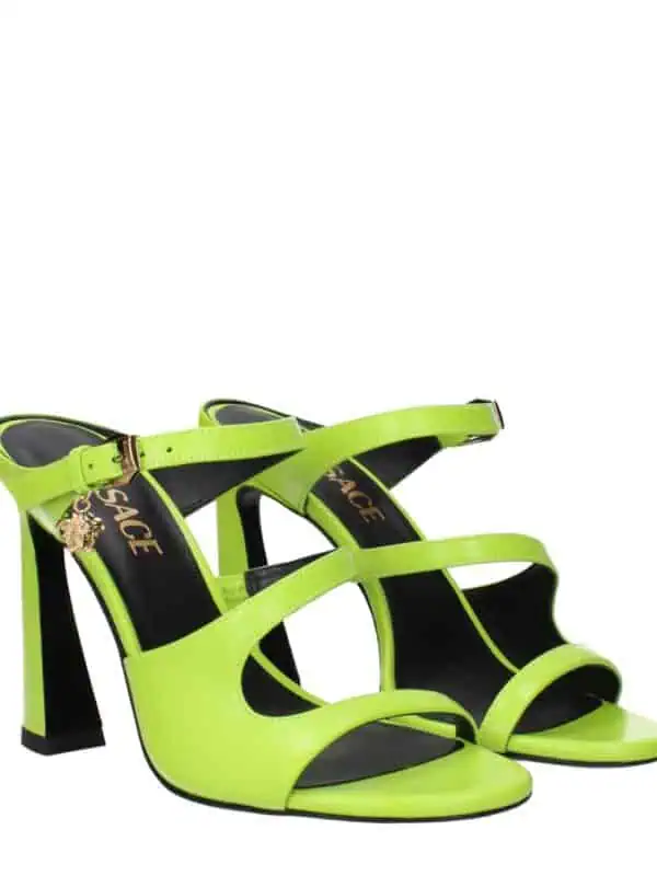 Neon yellow high-heeled sandals with ankle straps and gold lion charm, stylish and bold for luxury fashion statements.