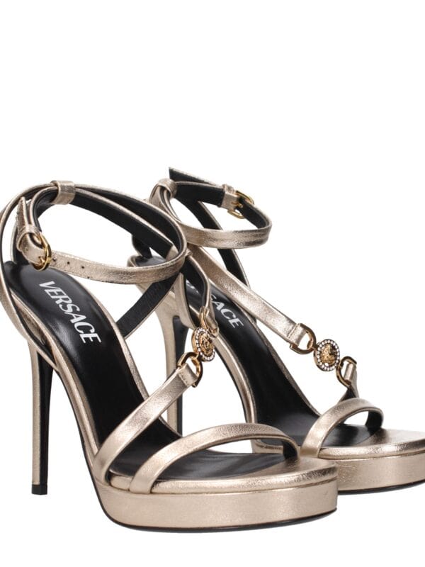 Elegant gold high-heeled sandals with ankle straps and Versace branding, featuring intricate embellishments and a sophisticated design for luxury fashion statements.