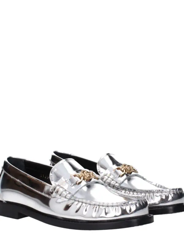 Reflective silver loafers with gold-tone emblem details, slip-on design, and black rubber soles, perfect for a luxurious and fashionable look.