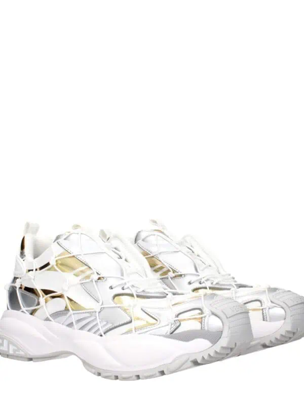 Reflective white and metallic gold designer sneakers with intricate web-like detailing and chunky soles for a bold luxury fashion statement.