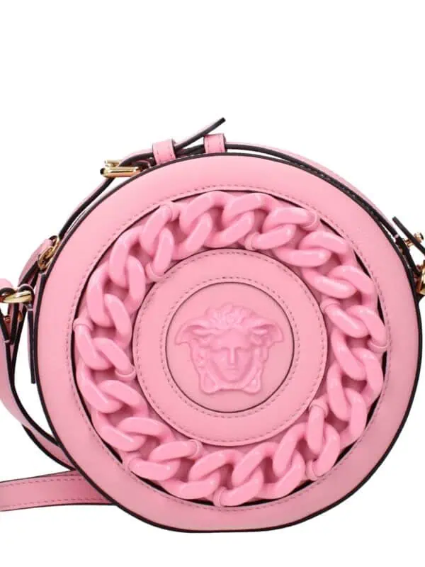 Pink round handbag with a prominent Medusa emblem and chunky chain detail, featuring a black strap and gold hardware, perfect for upscale fashion statements.