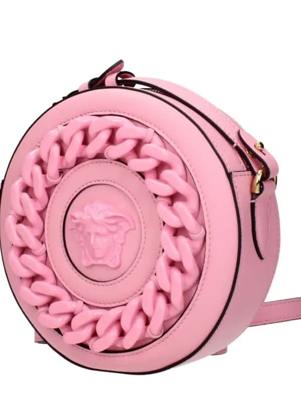 Pink round designer shoulder bag with a bold embossed Medusa head logo and chunky chain detail, perfect for a stylish and trendy look.