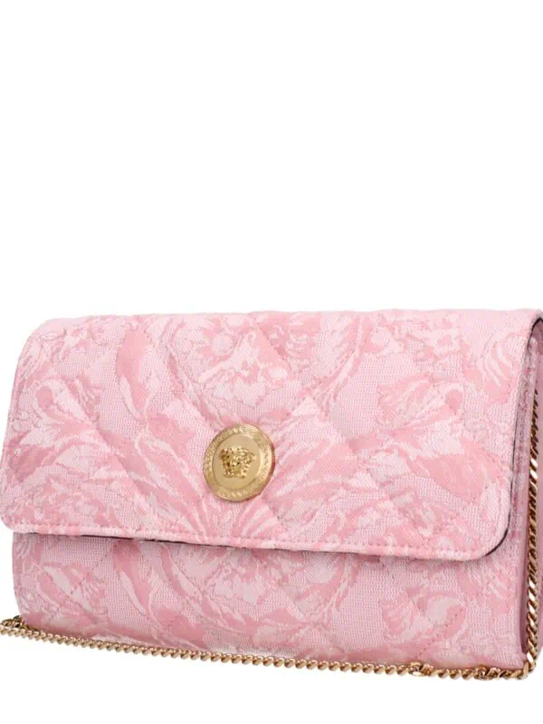 Elegant pink designer clutch with floral jacquard fabric, gold emblem detail, and chain strap, perfect for luxury evening events and special occasions.